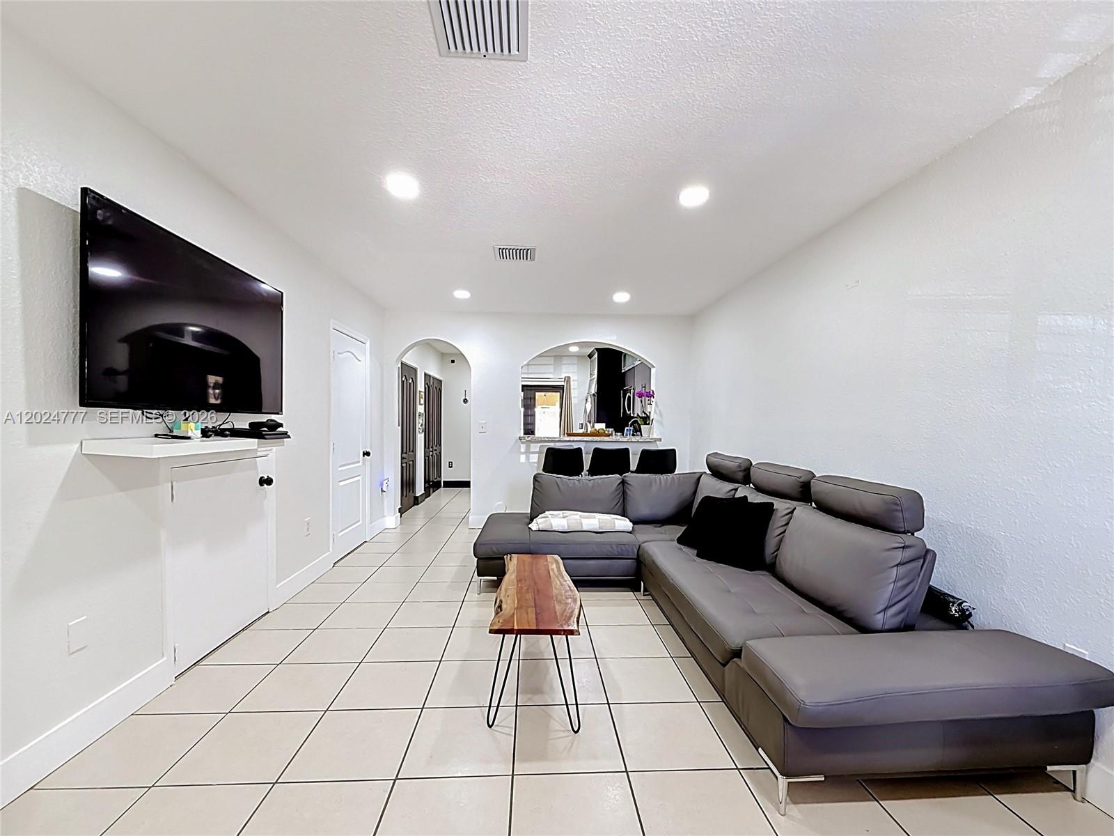 A living room features a grey sectional sofa, tiled floors, and a wall-mounted television — 7699 W 36th Ave # 1, Hialeah FL 33018, HIALEAH, FL