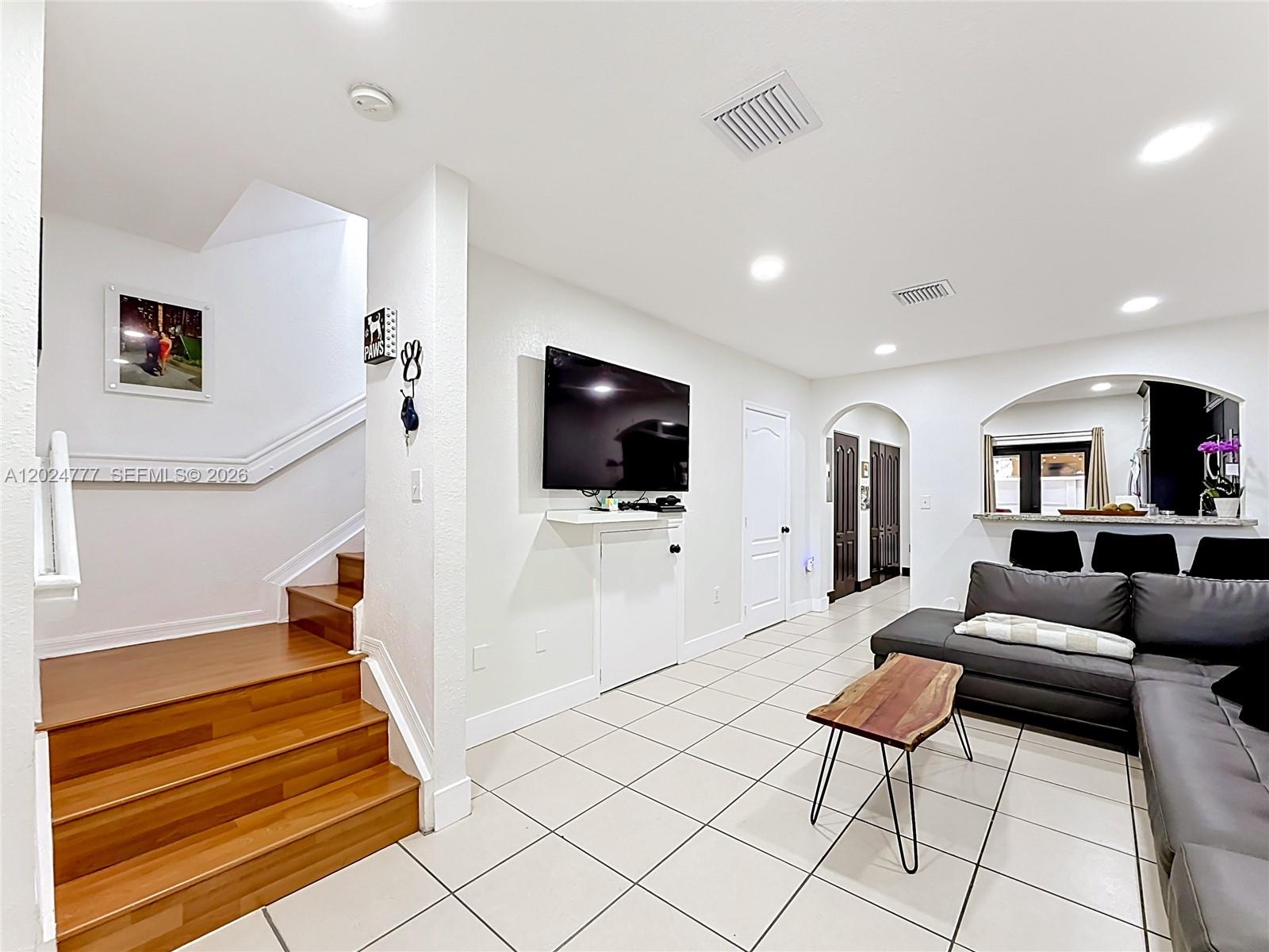 A living room features white walls, tile flooring, a wooden staircase, and a wall-mounted television — 7699 W 36th Ave # 1, Hialeah FL 33018, HIALEAH, FL