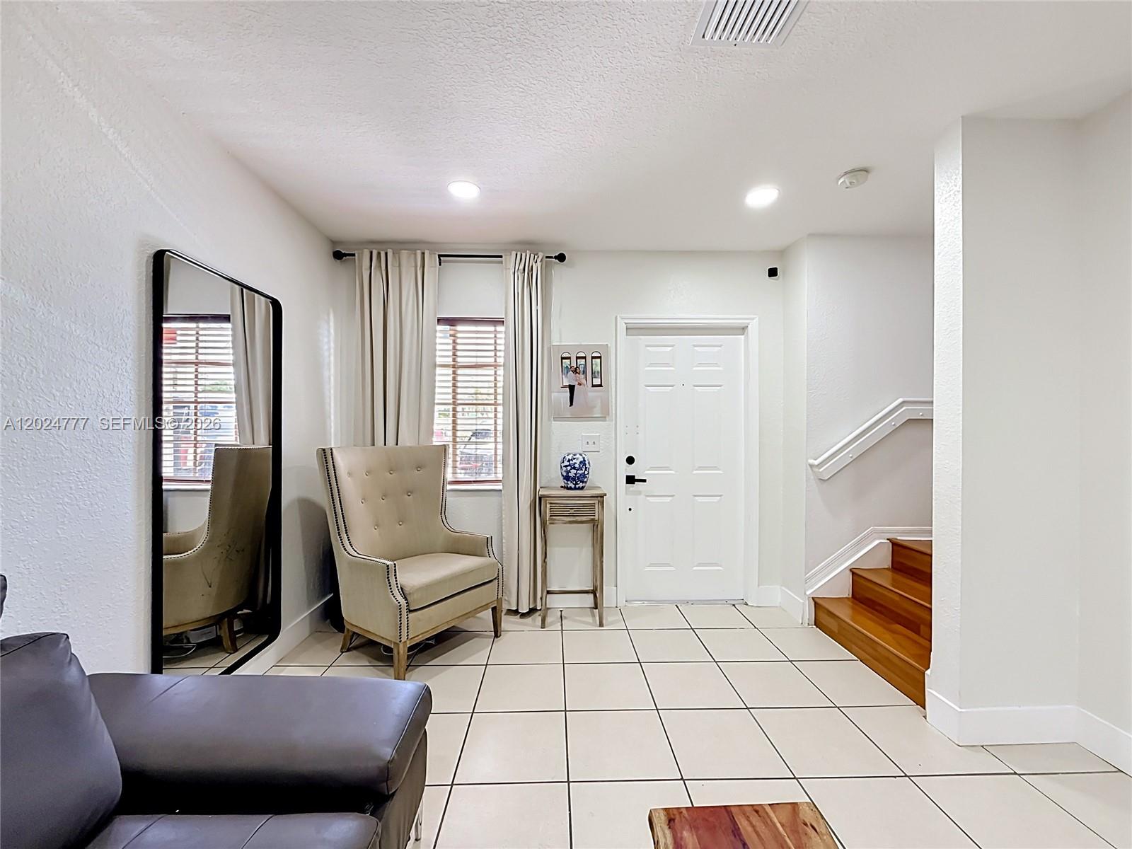 This entryway features a tiled floor, a beige armchair, a mirror, and a wooden staircase — 7699 W 36th Ave # 1, Hialeah FL 33018, HIALEAH, FL