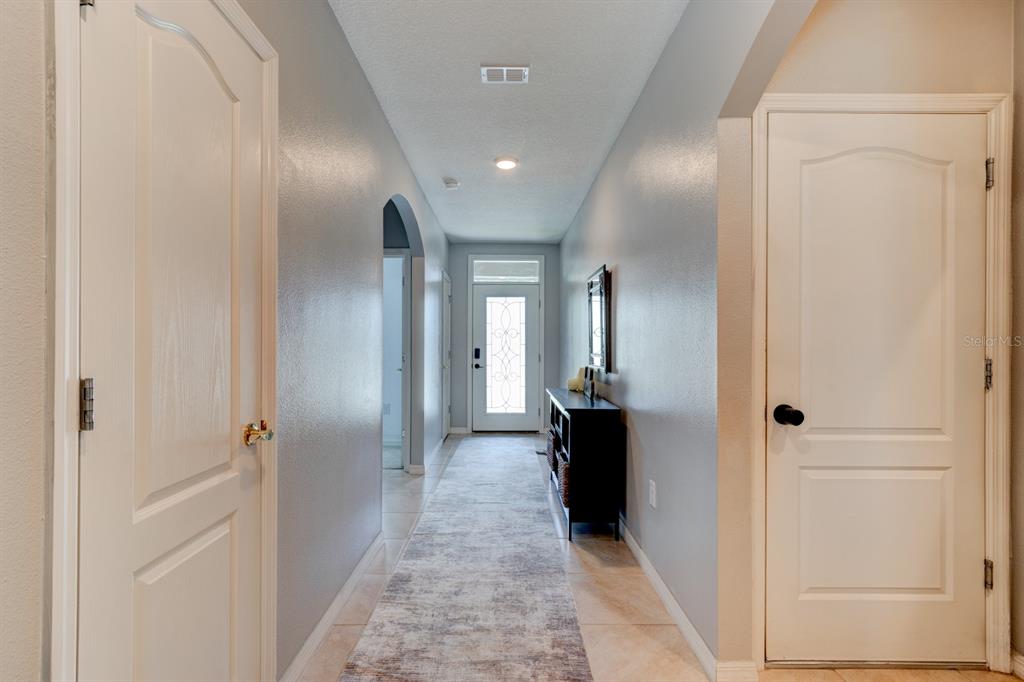 A hallway with light-colored tile flooring, gray walls, and white doors leads to an entryway — 1814 PALMETTO SCRUB CIRCLE, PORT ORANGE, FL