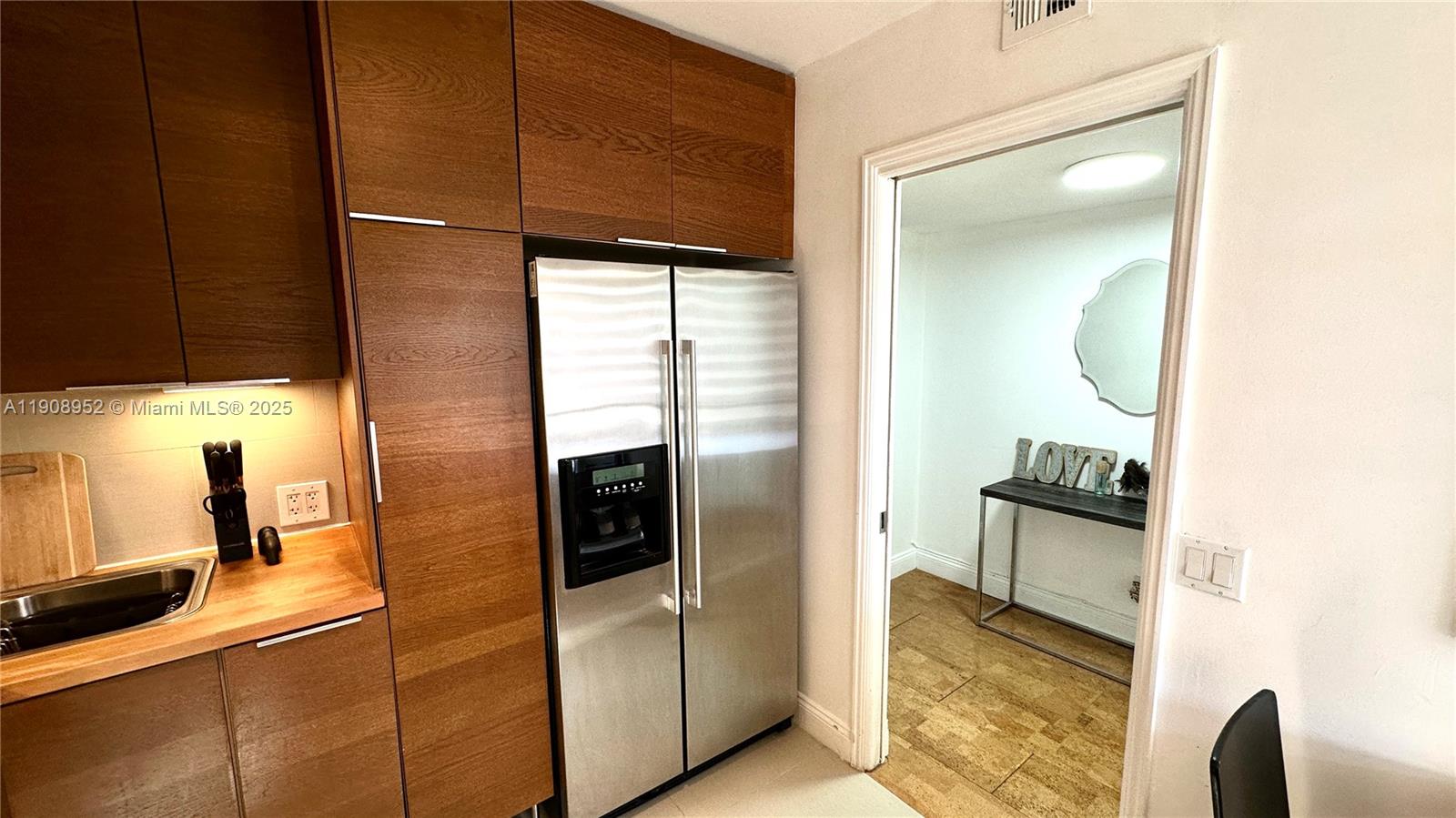 A kitchen features wood-toned cabinetry, a stainless steel refrigerator, and a doorway to another room — 2651 S Course Dr # 307, Pompano Beach FL 33069, POMPANO BEACH, FL