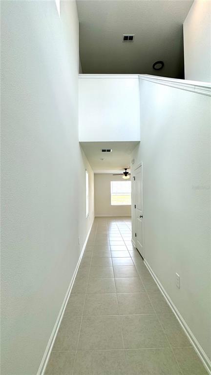 A long hallway with light-colored tile flooring leads toward a room with a ceiling fan — 3430 HOWELL DRIVE, LAKE WALES, FL