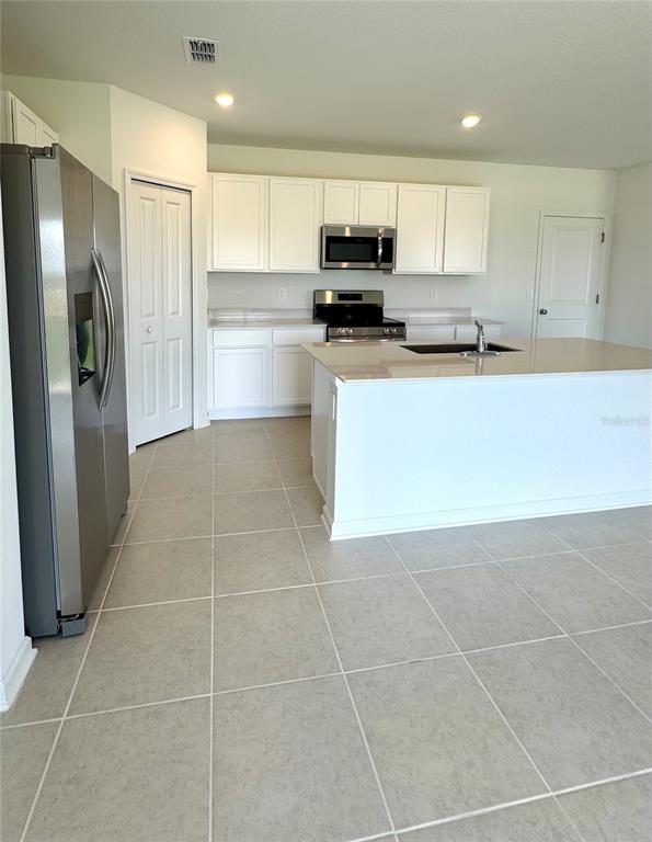 A kitchen features white cabinets, stainless steel appliances, a center island, and light tile flooring — 3430 HOWELL DRIVE, LAKE WALES, FL