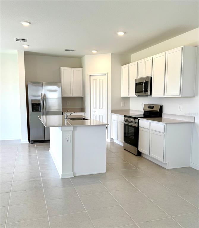 A kitchen features white cabinets, stainless steel appliances, a center island, and light tile flooring — 3430 HOWELL DRIVE, LAKE WALES, FL