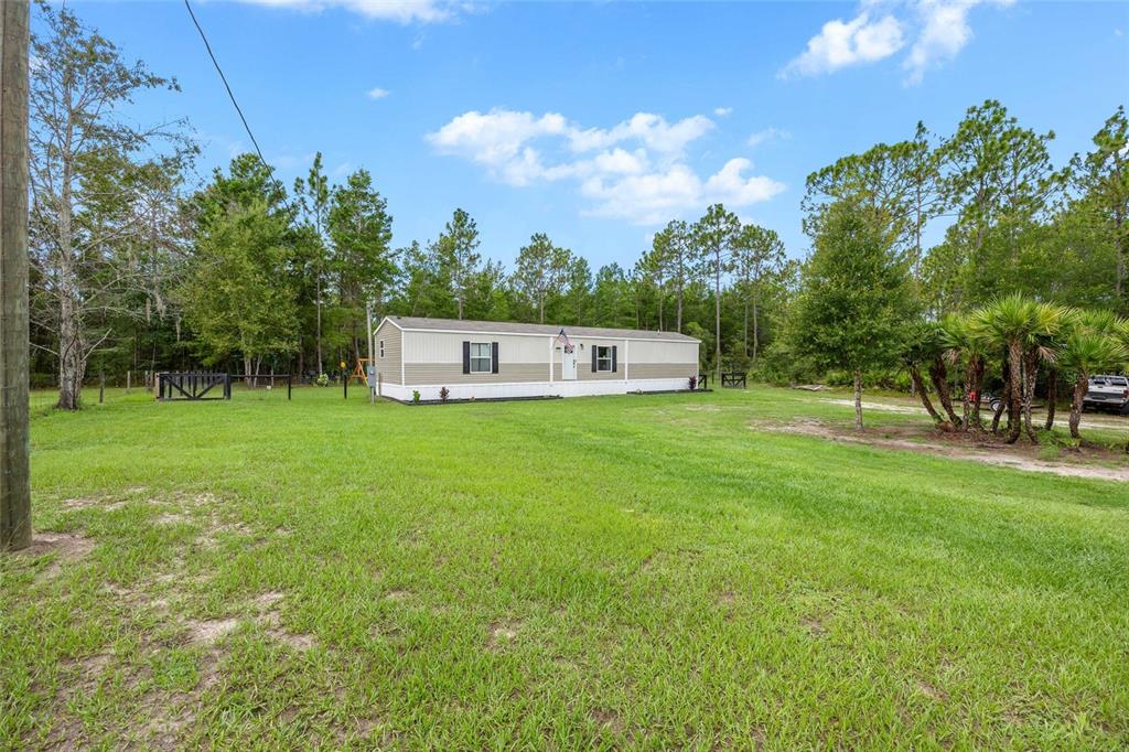 A single-story manufactured home sits on a large, grassy lot surrounded by trees — 8444 W JENNIFER COURT, CRYSTAL RIVER, FL
