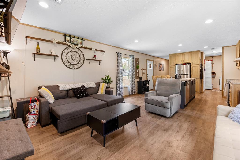 A living room with a gray sectional, a recliner, and an open kitchen with wood flooring — 8444 W JENNIFER COURT, CRYSTAL RIVER, FL