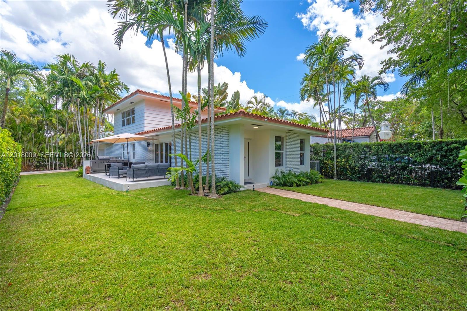 A two-story house with a white brick exterior, a patio, and palm trees in the yard — 1203 Madrid St, Coral Gables FL 33134, CORAL GABLES, FL