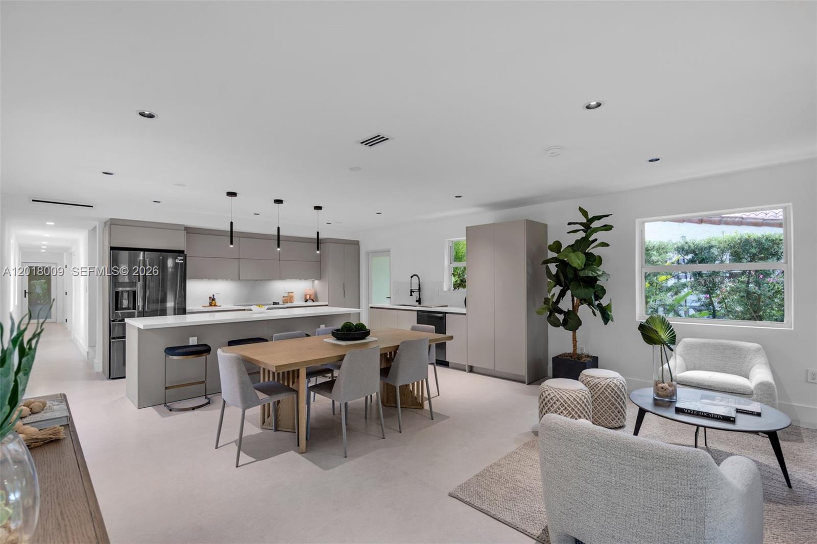 A modern open-concept kitchen and living area features light gray cabinetry and a wooden table — 1203 Madrid St, Coral Gables FL 33134, CORAL GABLES, FL