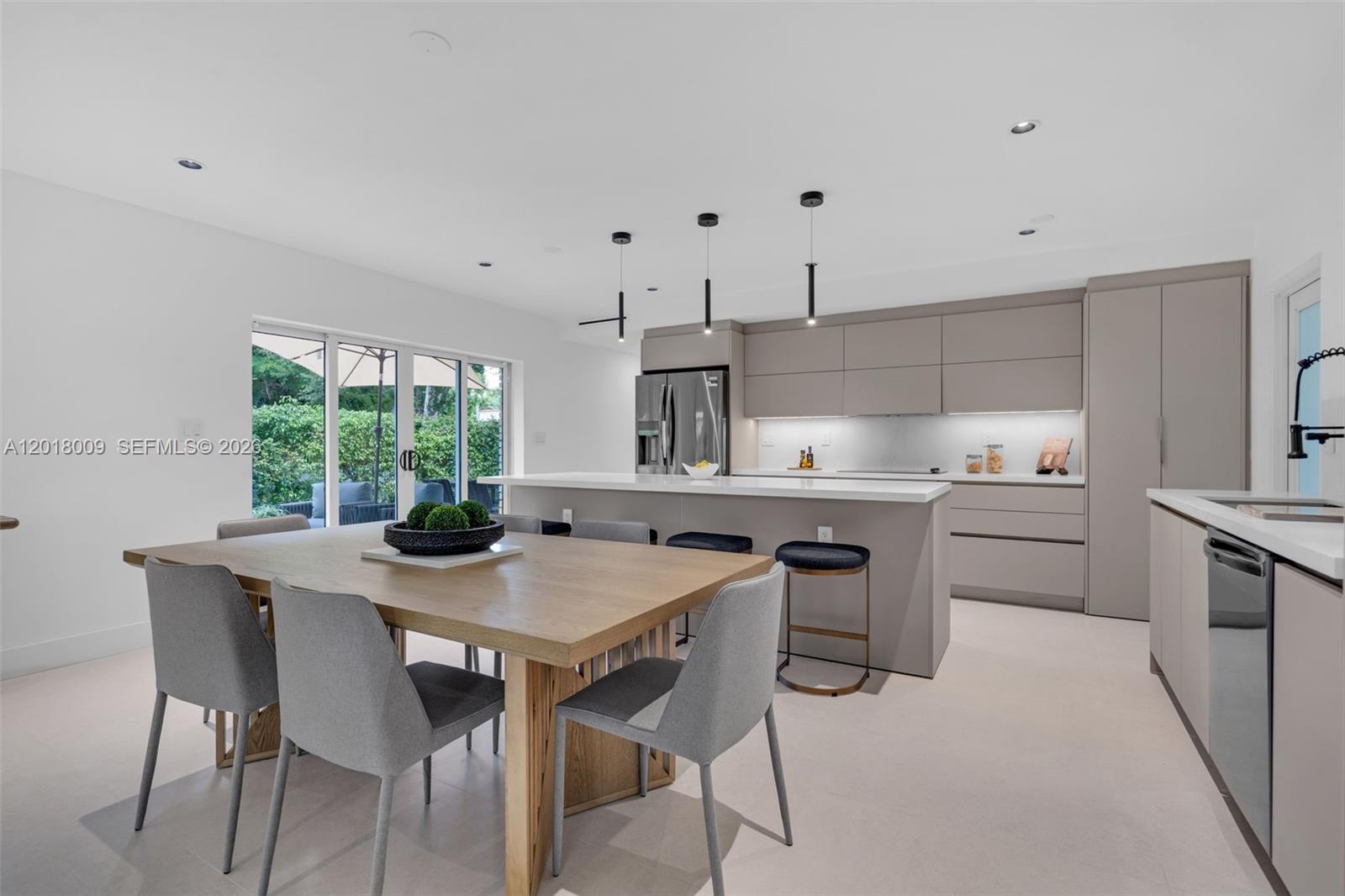 A modern kitchen features light gray cabinetry, a large island with bar seating, and dining area — 1203 Madrid St, Coral Gables FL 33134, CORAL GABLES, FL