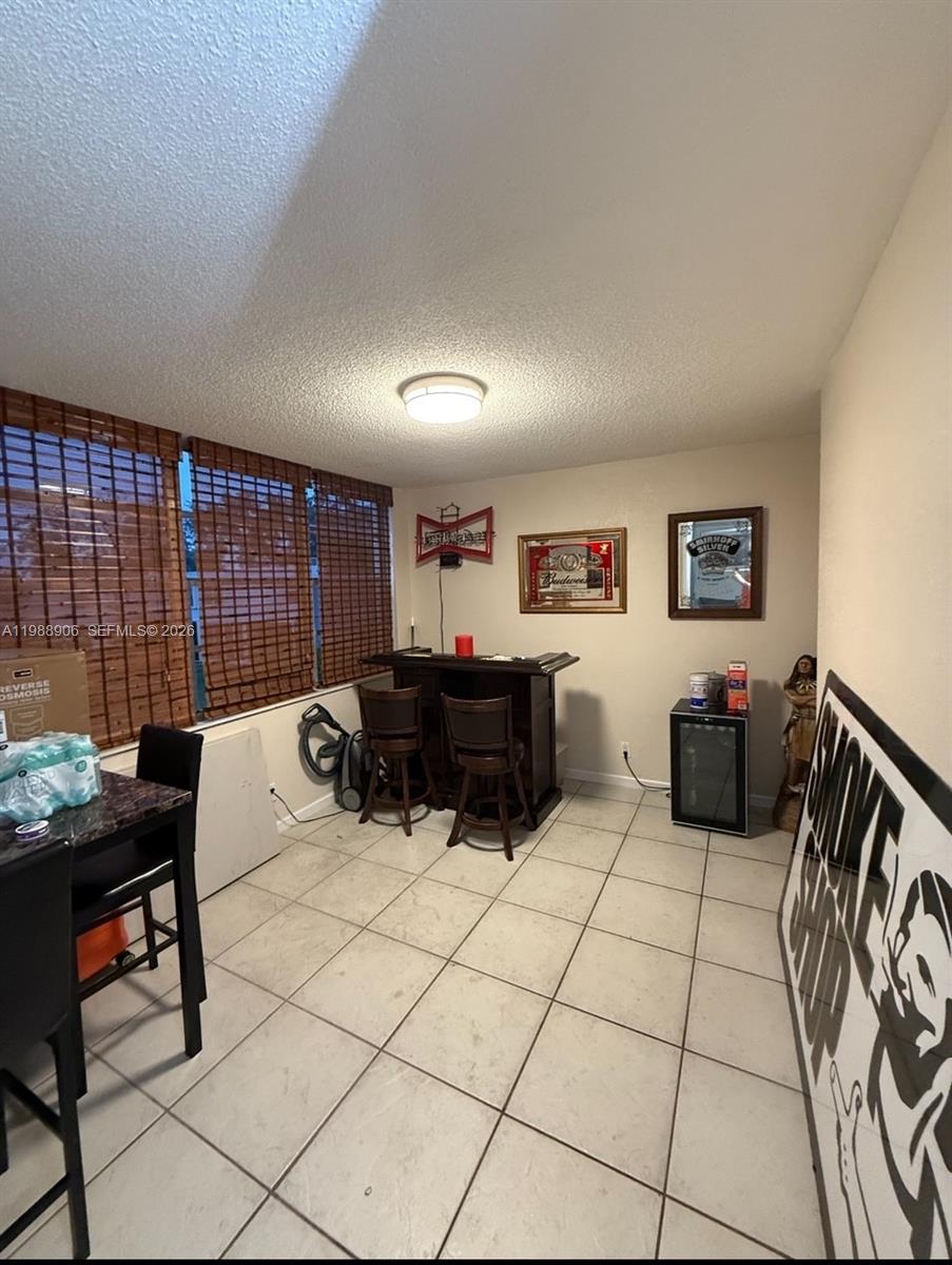An empty living room features beige tile flooring, white walls, and a sliding glass balcony door — 9441 Live Oak Pl # 209, Davie FL 33324, DAVIE, FL
