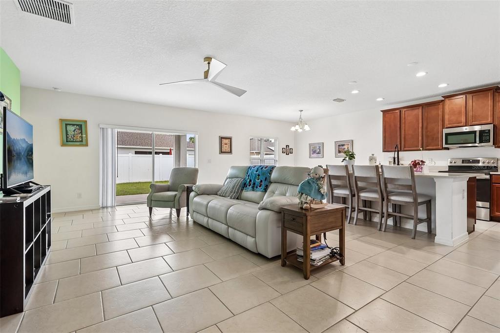 An open-concept living room and kitchen featuring tile flooring, a light-colored sofa, and sliding doors — 833 AVENAL LANE, DAVENPORT, FL