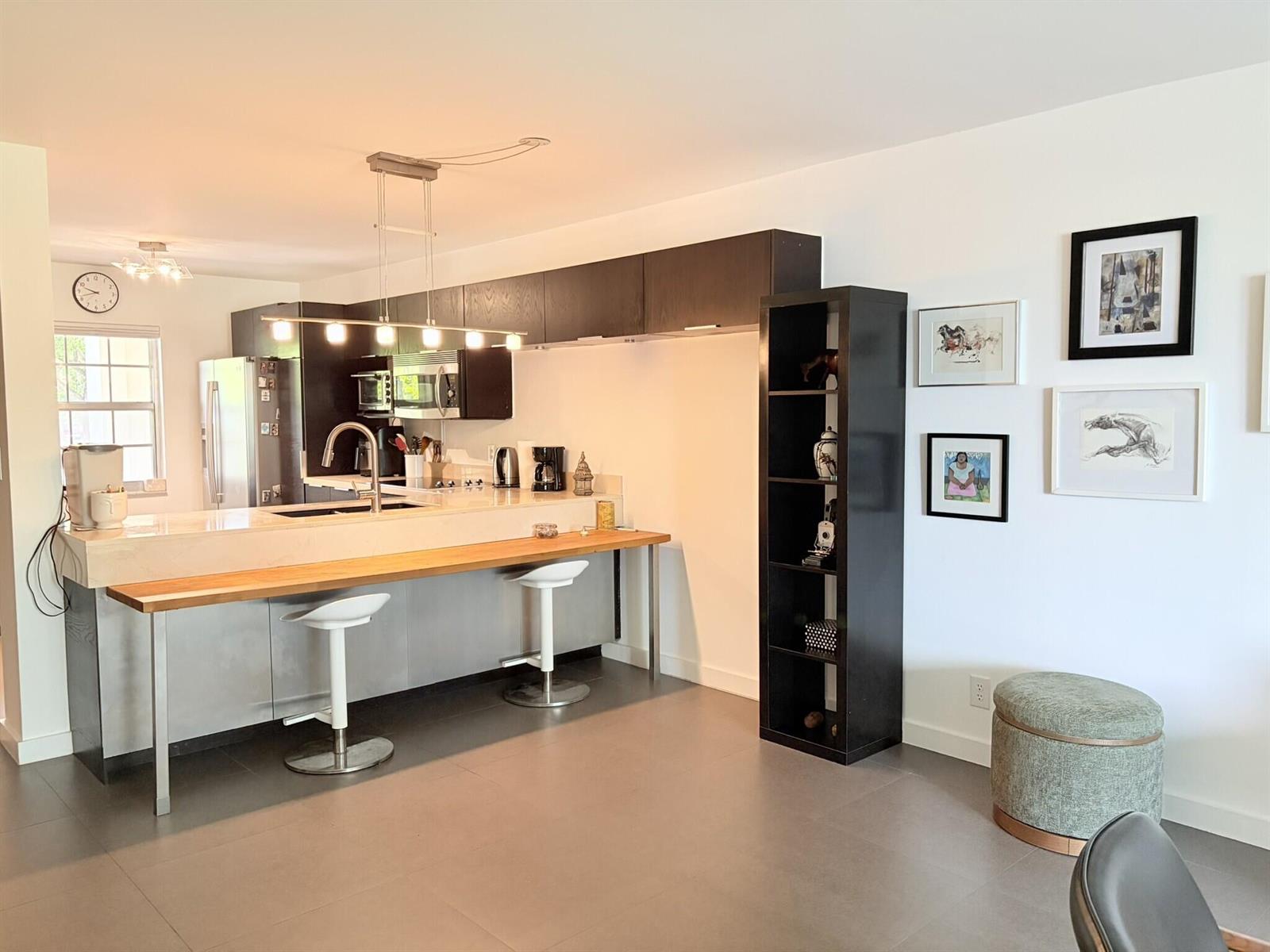 A modern kitchen features a breakfast bar, dark cabinetry, and a tall open shelving unit — 3503 Oaks Way # 202, Pompano Beach FL 33069, POMPANO BEACH, FL