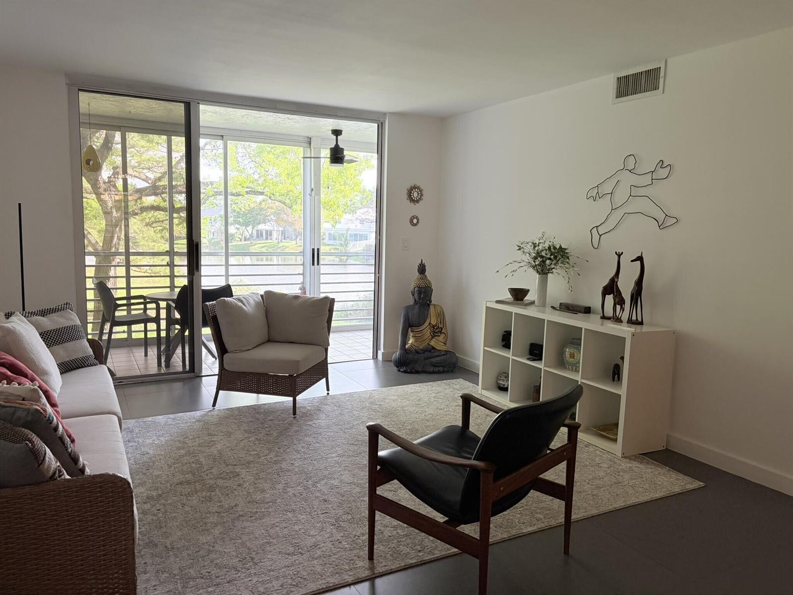 A living room with a white sofa, black accent chair, Buddha statue, and a sliding door — 3503 Oaks Way # 202, Pompano Beach FL 33069, POMPANO BEACH, FL