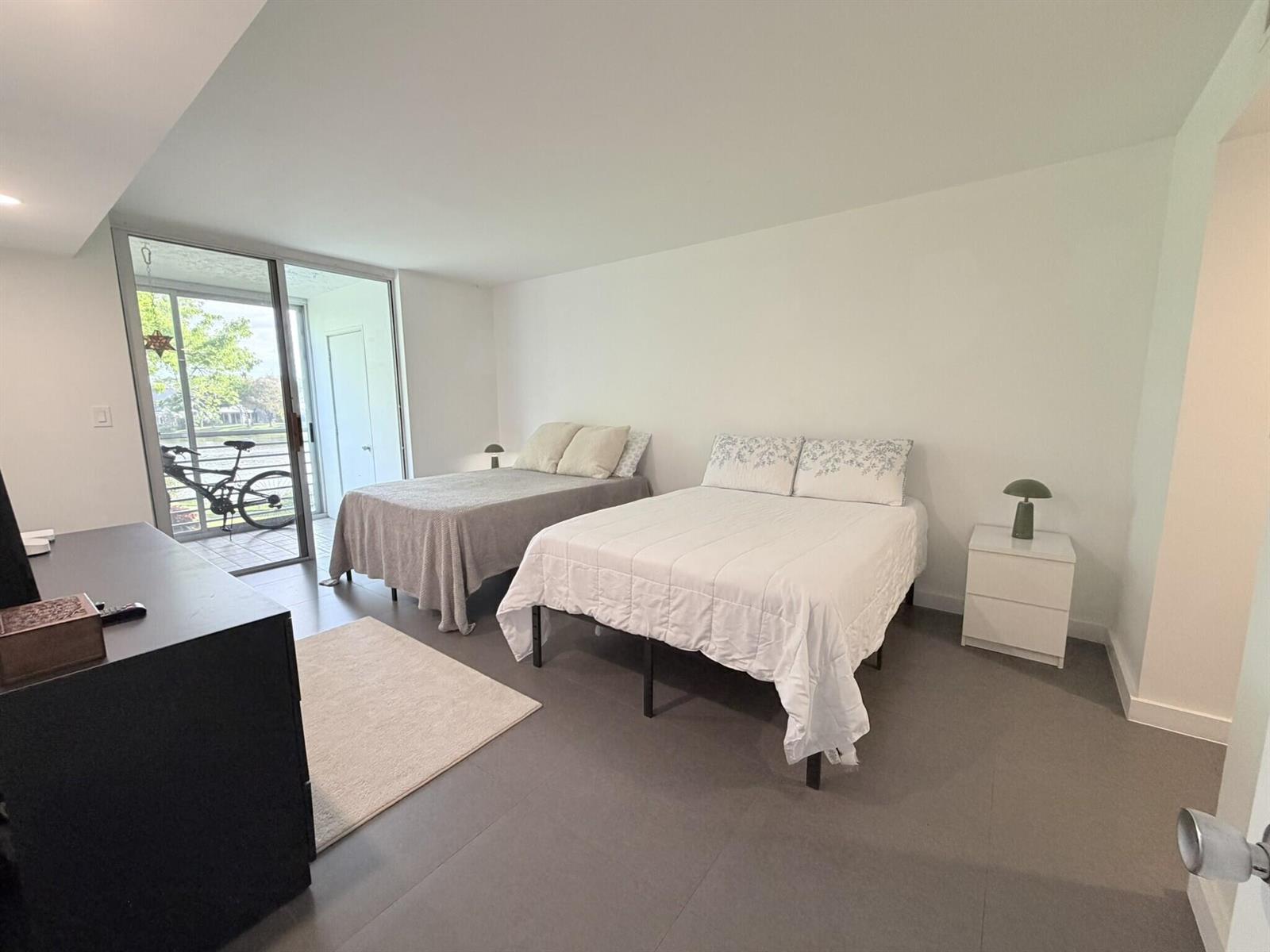 A bedroom features two beds, white walls, gray tile flooring, and a sliding glass door — 3503 Oaks Way # 202, Pompano Beach FL 33069, POMPANO BEACH, FL