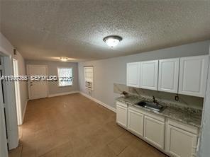 A kitchen with white cabinets and granite countertops opens into a living area — 820 21st St # C, West Palm Beach FL 33407, WEST PALM BEACH, FL