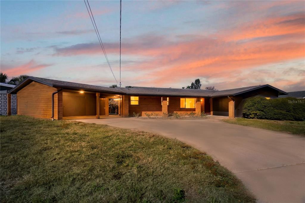 A single-story house with wood siding, a carport, and a concrete driveway at sunset — 1503 CANAL COURT, TAVARES, FL