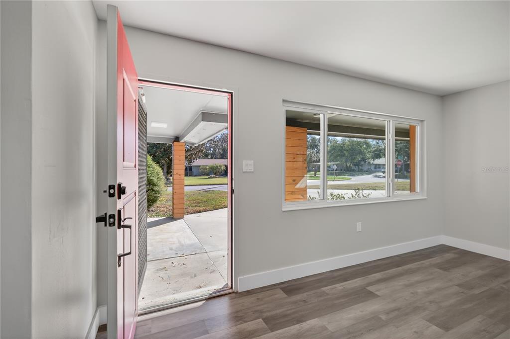 An interior view of an entryway featuring a red door, large window, and wood flooring — 1503 CANAL COURT, TAVARES, FL