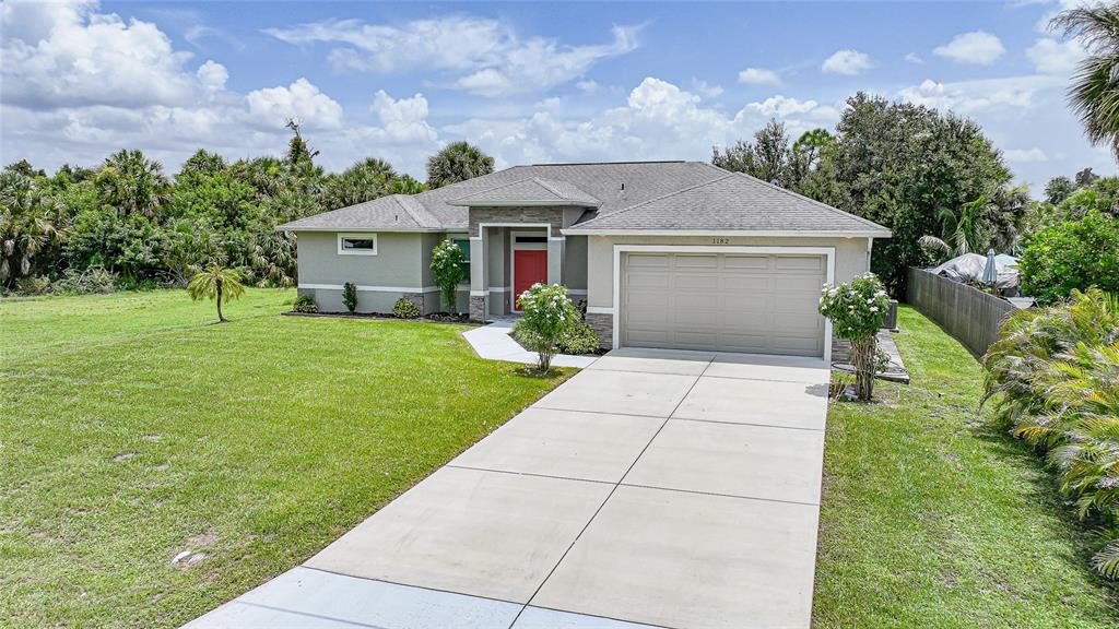 A single-story house with a beige exterior, a red front door, and a concrete driveway — 1182 YORKSHIRE STREET, PORT CHARLOTTE, FL