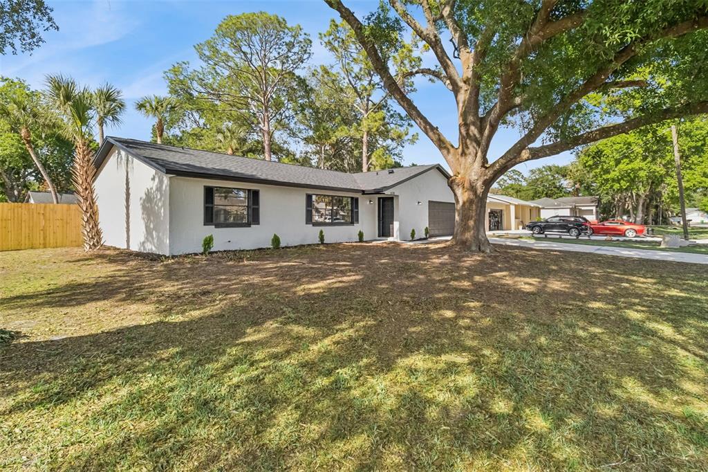 A white, single-story house with a dark roof and a large tree in the yard — 5170 ANDOVER STREET, COCOA, FL