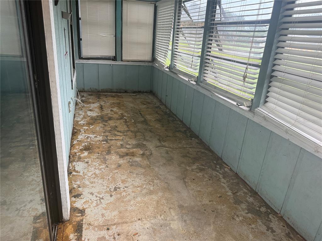 An enclosed porch features light blue paneled walls, white blinds, and a worn concrete floor — 1116 FAIRVILLA DRIVE UNIT 1116, NEW SMYRNA BEACH, FL