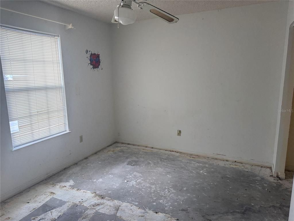 An empty bedroom features white walls, a ceiling fan, a window with blinds, and unfinished flooring — 1116 FAIRVILLA DRIVE UNIT 1116, NEW SMYRNA BEACH, FL