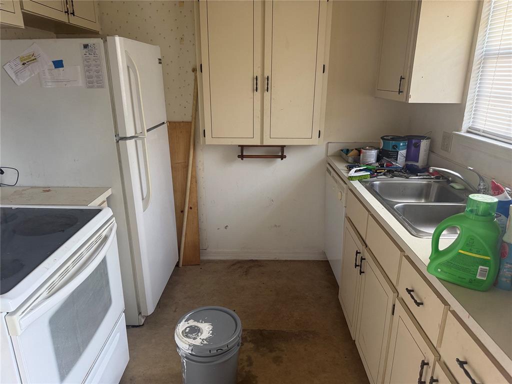 A kitchen features white appliances, light-colored cabinets, a double sink, and a worn floor — 1116 FAIRVILLA DRIVE UNIT 1116, NEW SMYRNA BEACH, FL