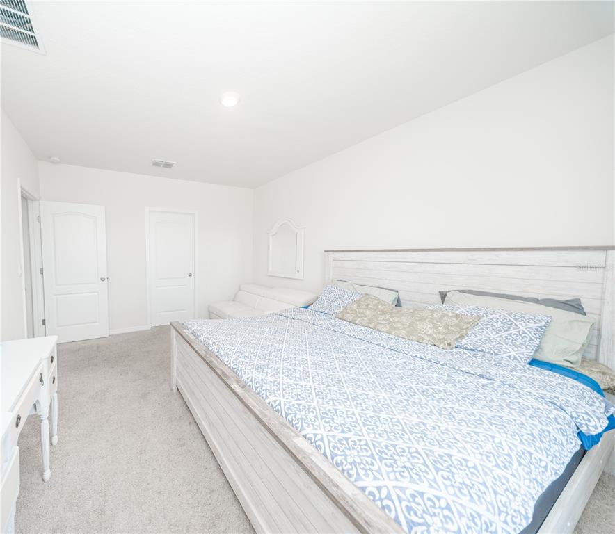 A bedroom features a large bed with a patterned comforter, white furniture, and carpeted flooring — 3838 WHITNEY WAY, HAINES CITY, FL