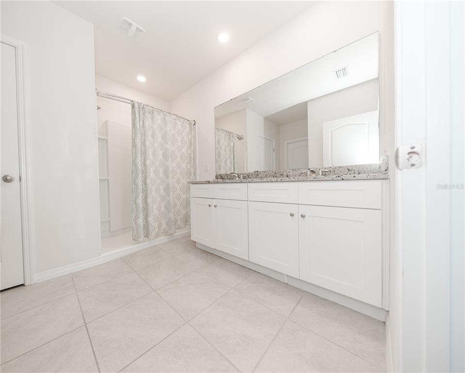 A bathroom features a white double vanity with a granite countertop and a shower stall — 3838 WHITNEY WAY, HAINES CITY, FL