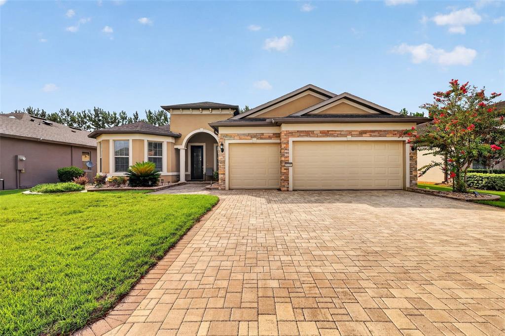 A single-story suburban house with a paved driveway, three-car garage, and stone facade accents — 9199 SW 70TH LOOP, OCALA, FL