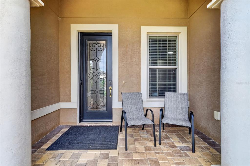 A covered front porch features a dark glass-paneled door, two gray chairs, and paver flooring — 9199 SW 70TH LOOP, OCALA, FL