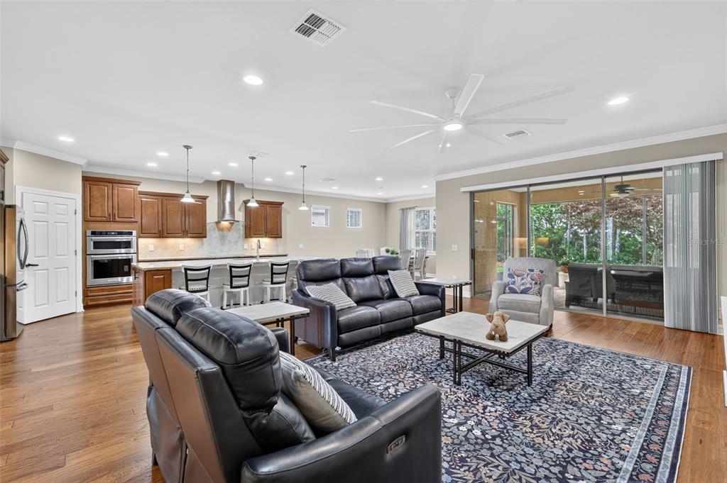 An open-concept living room and kitchen with dark leather furniture, hardwood floors, and sliding doors — 9199 SW 70TH LOOP, OCALA, FL