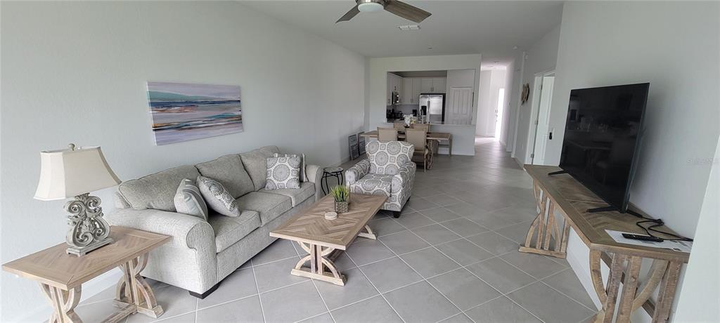 A living room features a sofa, patterned armchair, coffee table, and television on a console table — 8716 SAINT KITTS CIRCLE, ENGLEWOOD, FL
