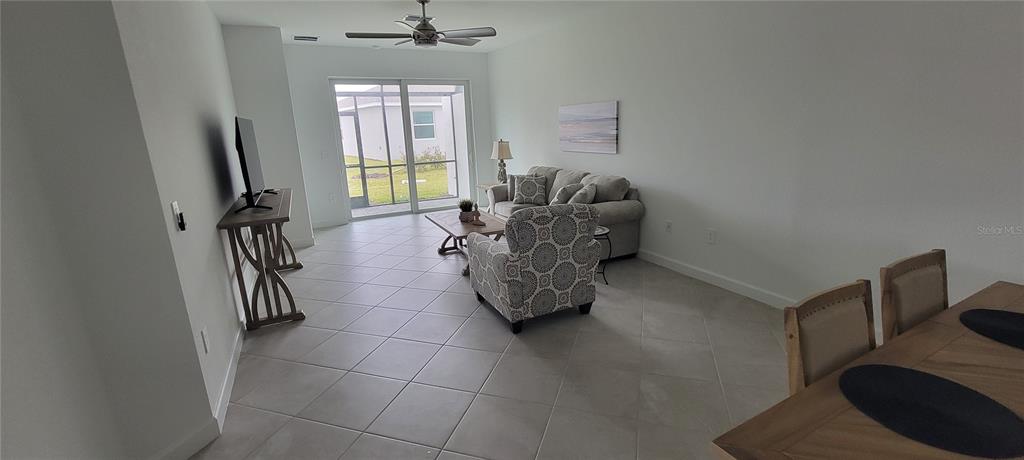 A living room with tile floors, a patterned armchair, a sofa, and a sliding glass door — 8716 SAINT KITTS CIRCLE, ENGLEWOOD, FL