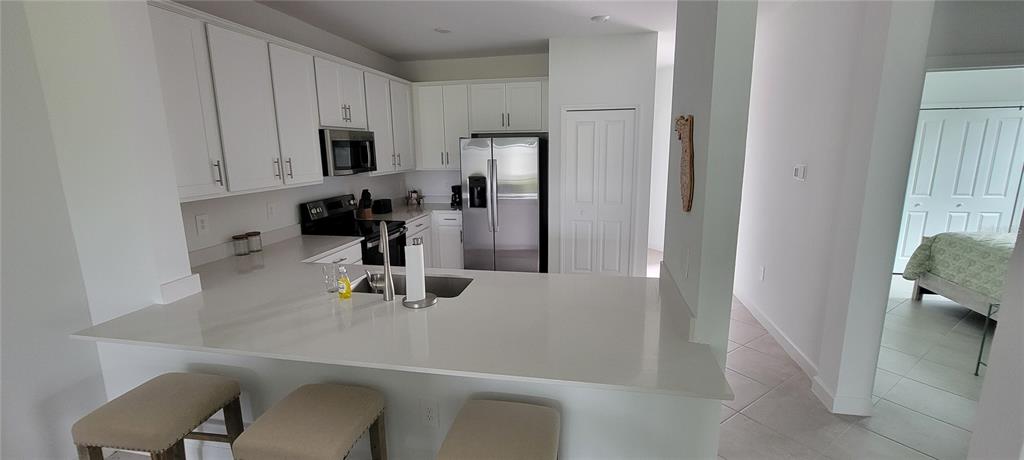 A kitchen features white cabinets, stainless steel appliances, and a quartz countertop breakfast bar — 8716 SAINT KITTS CIRCLE, ENGLEWOOD, FL