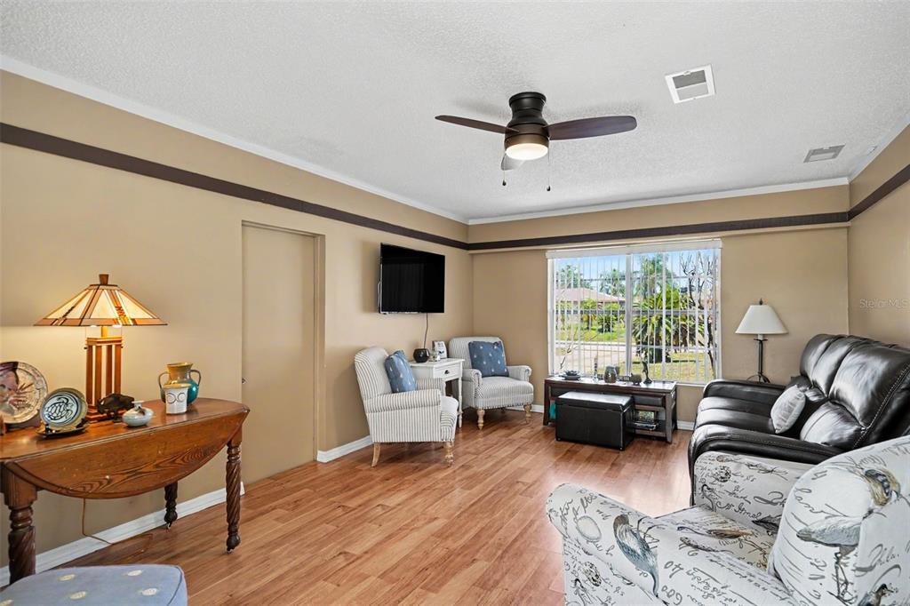A living room features wood-look flooring, a ceiling fan, a television, and assorted seating furniture — 250 CAMBRIDGE AVENUE NE, PALM BAY, FL