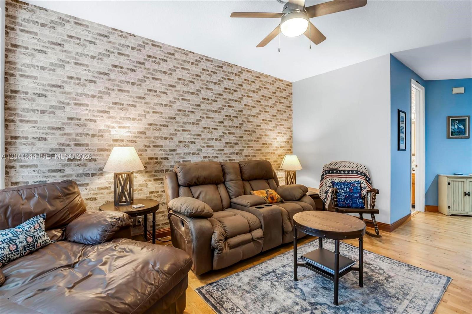 A living room features a faux brick accent wall, brown leather furniture, and a ceiling fan — 126 Spruce St, Boynton Beach FL 33426, BOYNTON BEACH, FL
