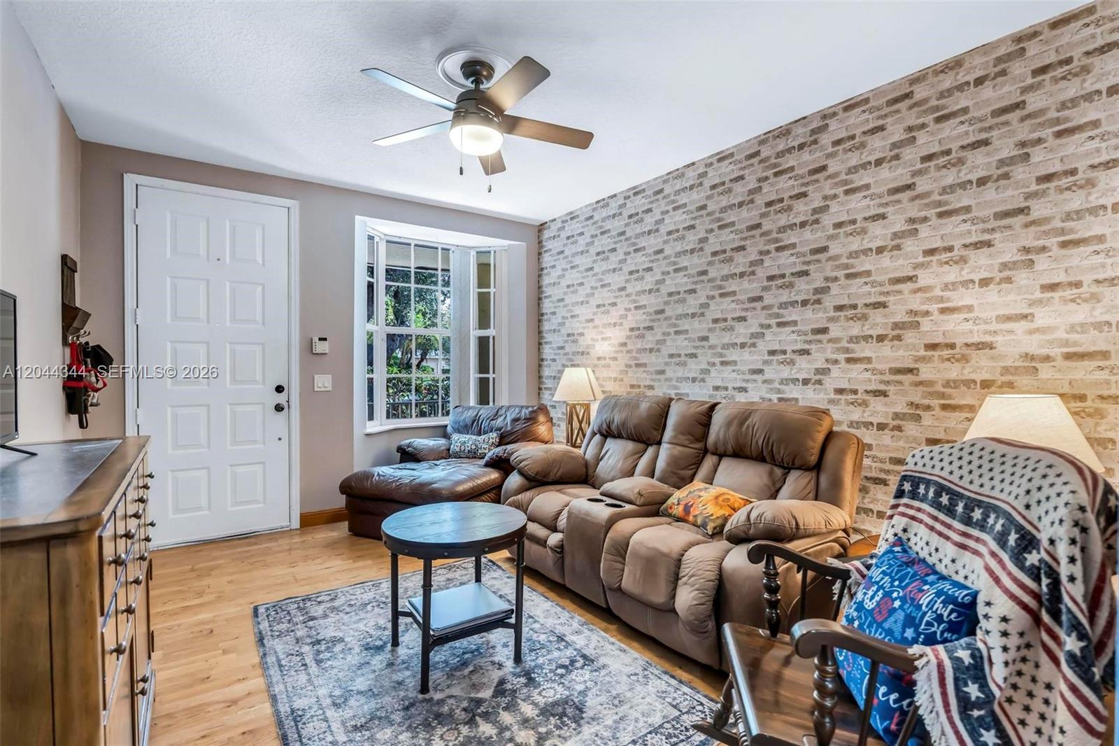 A living room features a brick accent wall, brown reclining sofa, and a ceiling fan — 126 Spruce St, Boynton Beach FL 33426, BOYNTON BEACH, FL