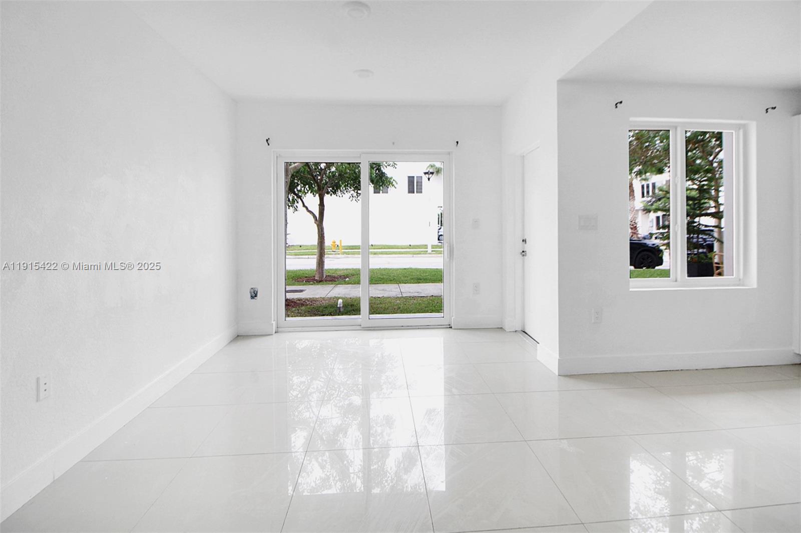 A bright, empty room features white walls, large glossy floor tiles, and a sliding glass door — 14482 SW 259th St, Homestead FL 33032, HOMESTEAD, FL