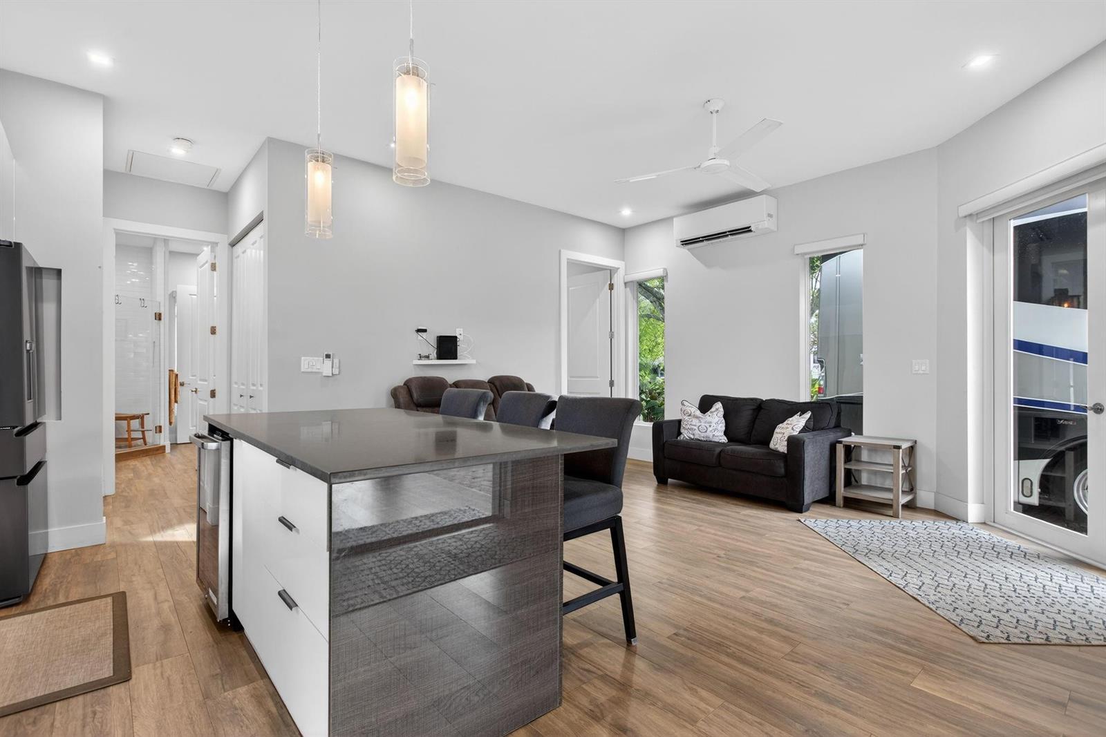 A modern kitchen island with bar stools faces a living area with a dark sofa — 119 S Cortez Drive # 119, Margate FL 33068, MARGATE, FL
