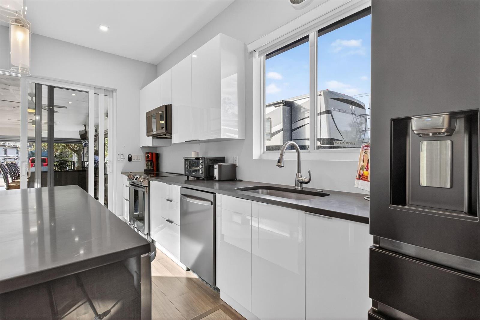 A modern kitchen features white glossy cabinets, dark countertops, stainless steel appliances, and a window — 119 S Cortez Drive # 119, Margate FL 33068, MARGATE, FL