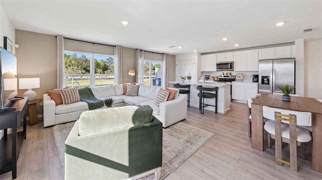 An open-concept living room and kitchen feature white cabinets, wood flooring, and a sectional sofa — 542 REMICK STREET, OSTEEN, FL