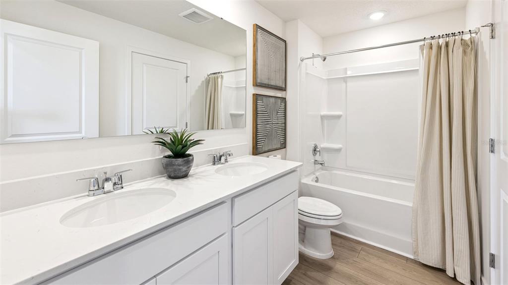 A bathroom features a double vanity with white cabinets, a mirror, and a shower-tub combo — 542 REMICK STREET, OSTEEN, FL