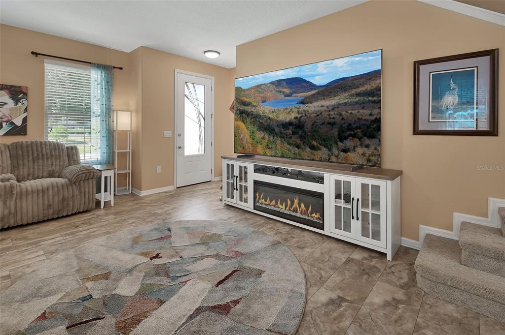 A living room features a large television on a fireplace console, tile flooring, and stairs — 337 ORCHARD HILL STREET, DELAND, FL