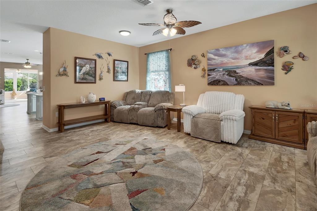 A living room features tile flooring, a circular rug, a ceiling fan, and coastal decor — 337 ORCHARD HILL STREET, DELAND, FL