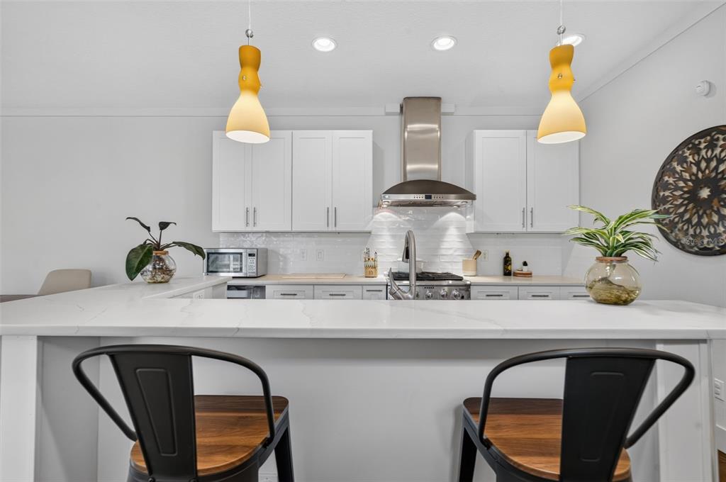 A modern kitchen features white cabinets, a quartz countertop, and two bar stools — 1071 ARAGON AVENUE, WINTER PARK, FL