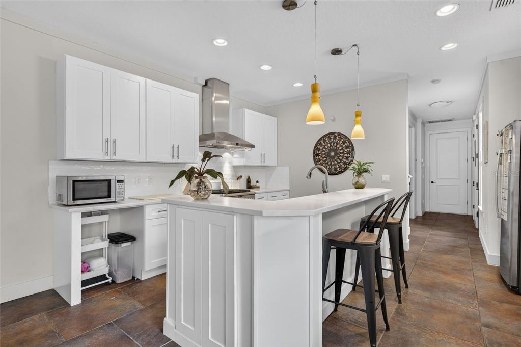 A modern kitchen features white cabinets, a quartz-topped island with bar stools, and tile flooring — 1071 ARAGON AVENUE, WINTER PARK, FL