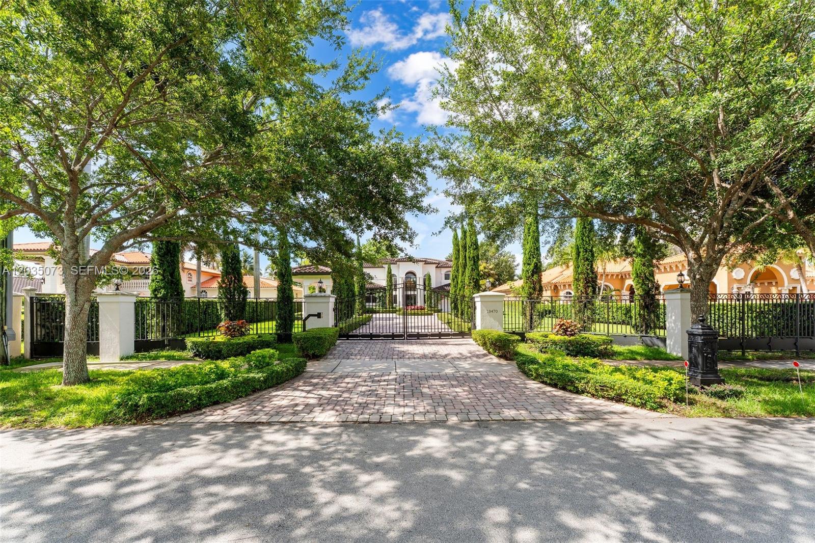 A gated driveway leads to a large white house framed by trees and manicured landscaping — 13470 SW 32nd St, Miami FL 33175, MIAMI, FL