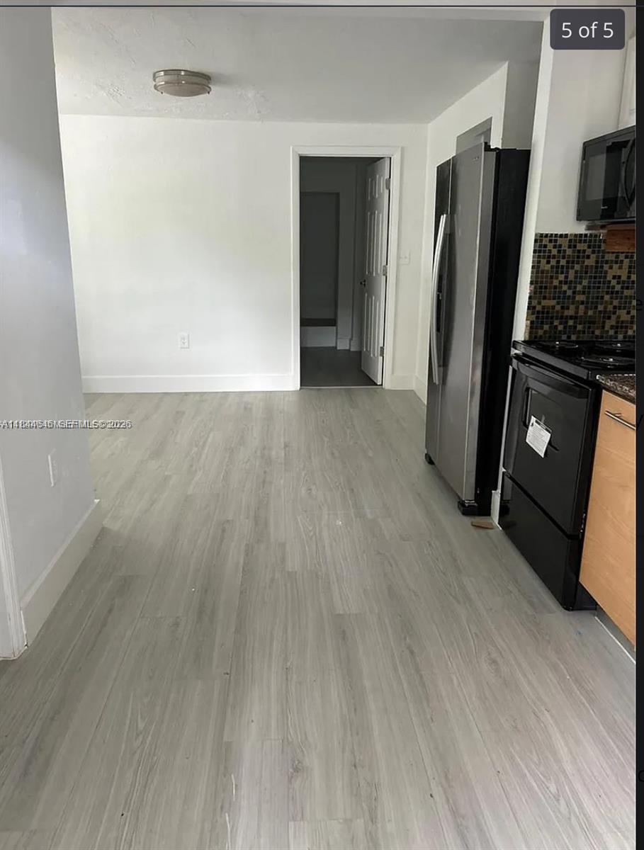 A kitchen with light wood-look flooring, stainless steel refrigerator, black stove, and a doorway beyond — 2215 NW 33rd St, Miami FL 33142, MIAMI, FL
