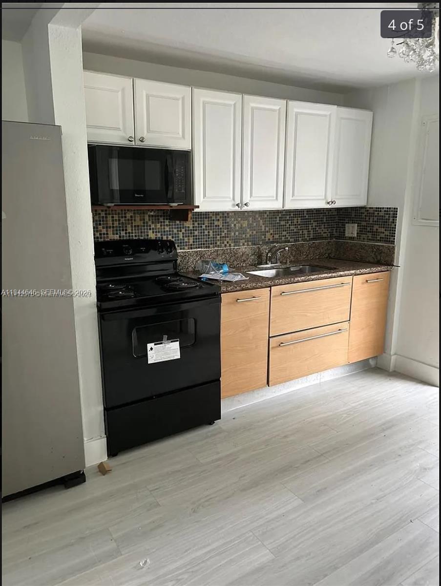 A kitchen features white upper cabinets, light wood lower cabinets, black appliances, and a mosaic backsplash — 2215 NW 33rd St, Miami FL 33142, MIAMI, FL