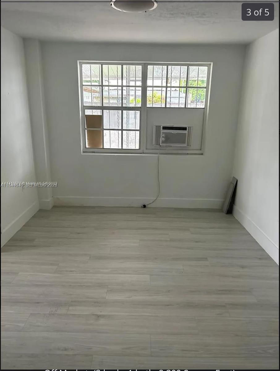 An empty room with light wood-look flooring, white walls, a window, and a wall-mounted AC — 2215 NW 33rd St, Miami FL 33142, MIAMI, FL
